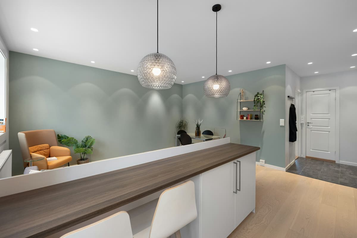 Empfang mit Holztheke, zwei Pendelleuchten und einem Sessel vor salbeigrüner Wand