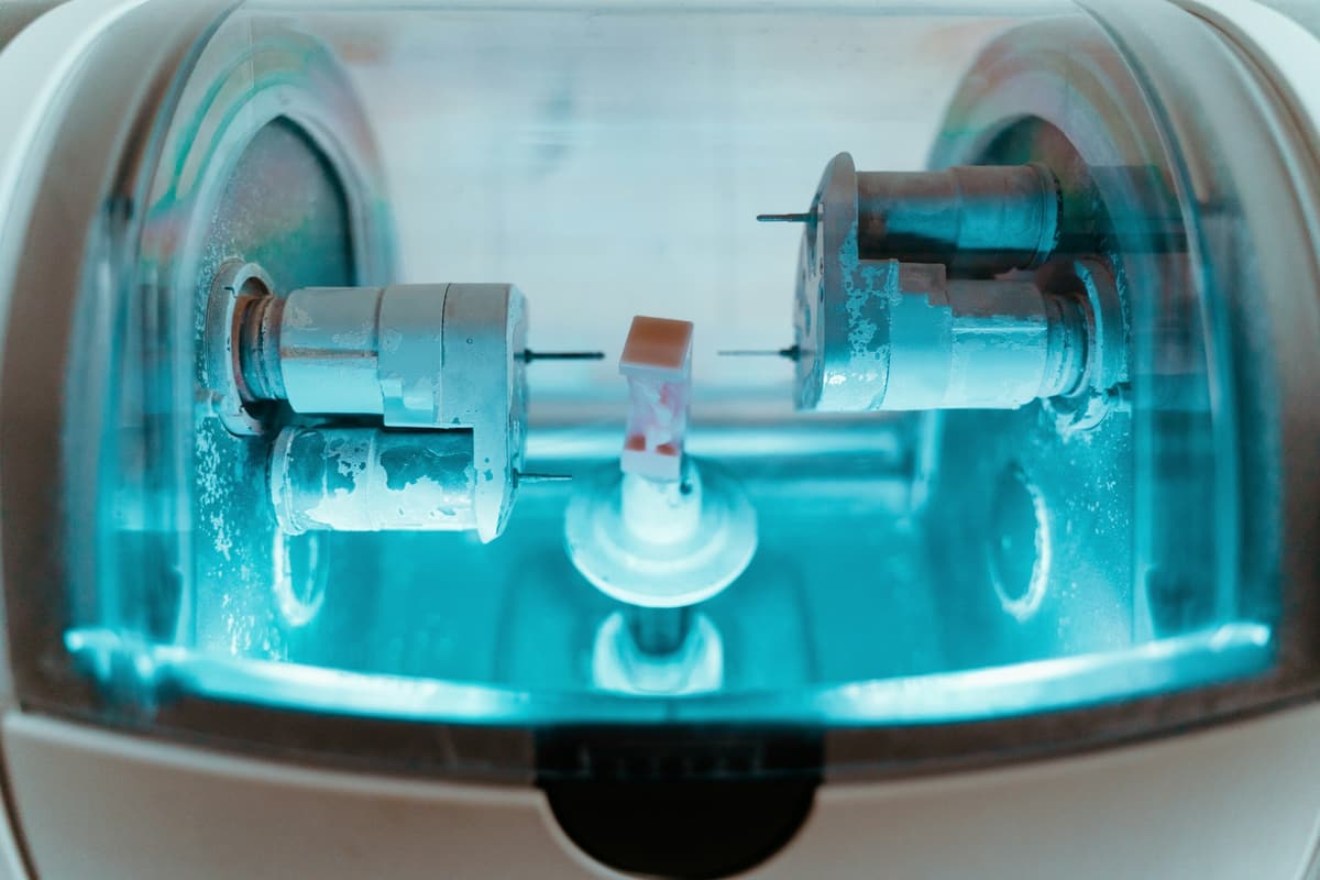 Fräsmaschine im Dentallabor, blau beleuchtet, mit einem Kronenrohling in der Halterung