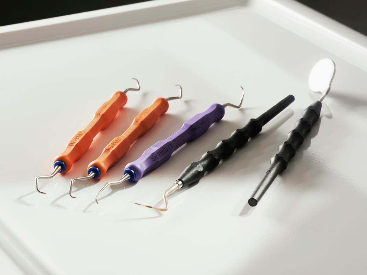 Fünf Handinstrumente mit orangen, violetten und schwarzen Griffen auf weißer Ablage